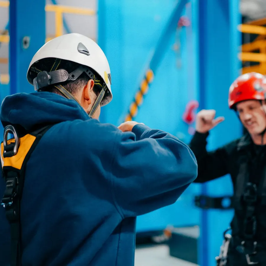 Tournage sur un chantier de structures, vidéaste en casque blanc face à un travailleur harnaché