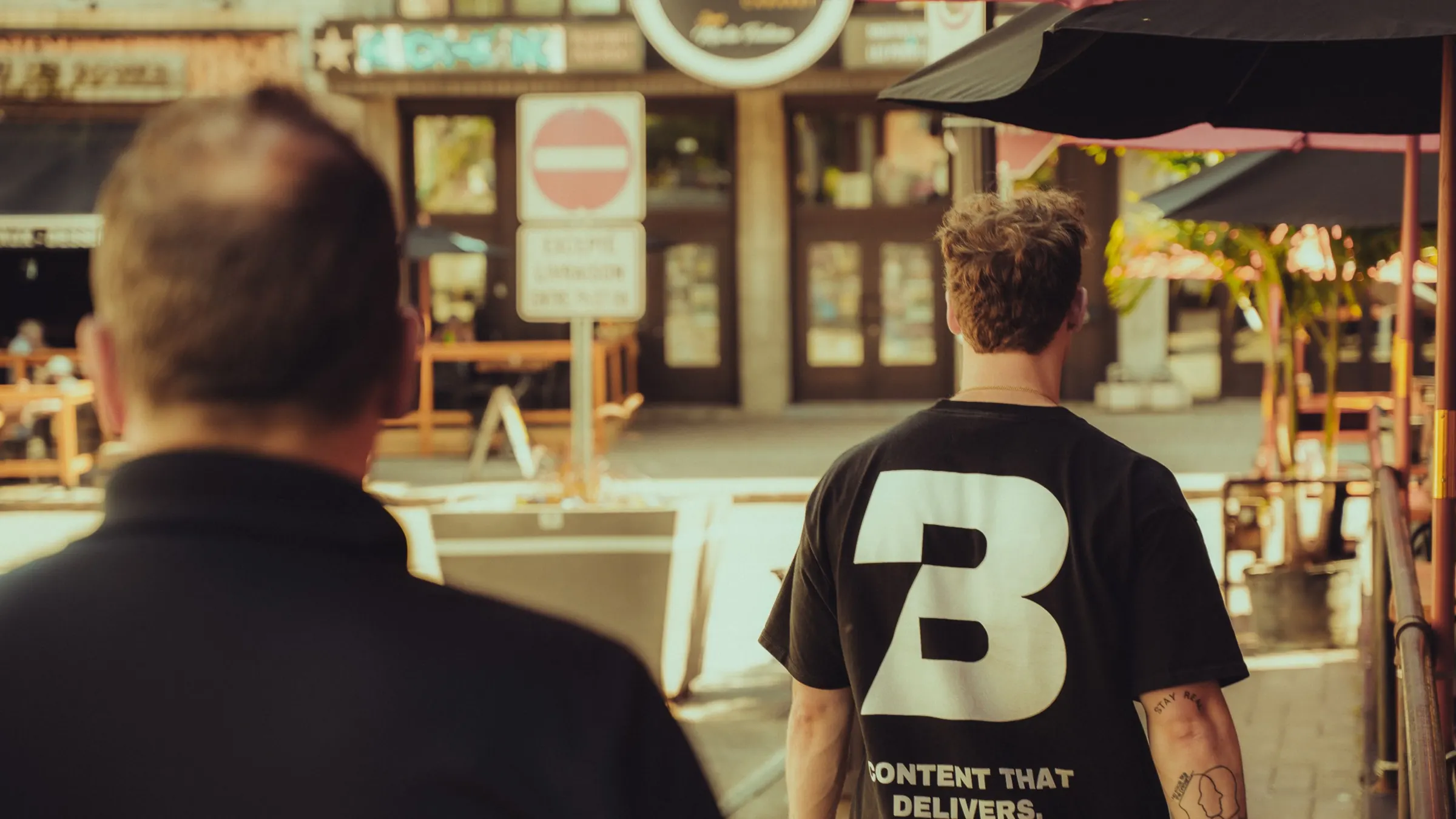 Deux membres de l'équipe Bolt Media de dos, en tournage sur une terrasse, chandail « Content that delivers »